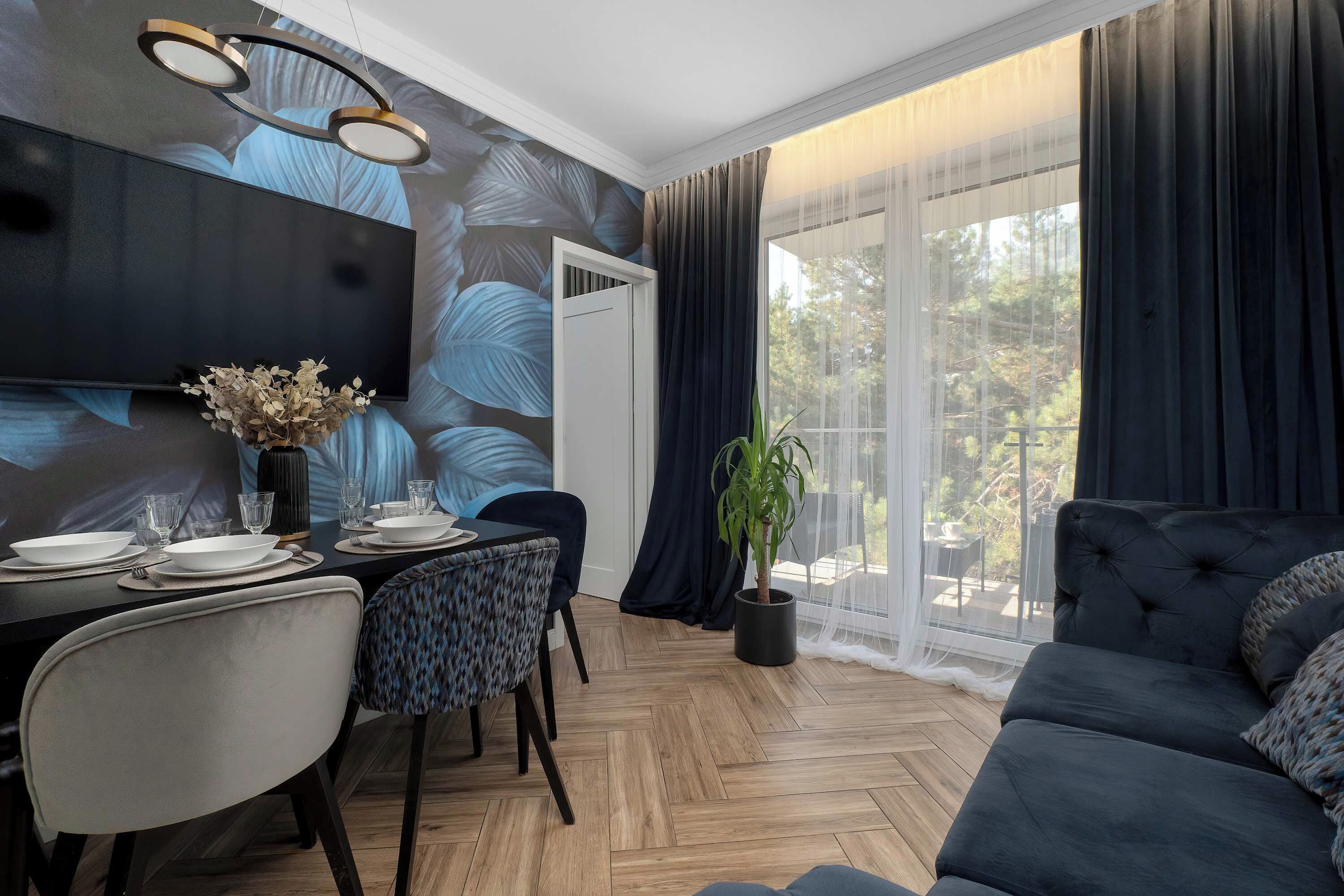 Uma zona de refeições moderna com uma mesa posta para quatro pessoas, um sofá e uma janela grande com cortinas.