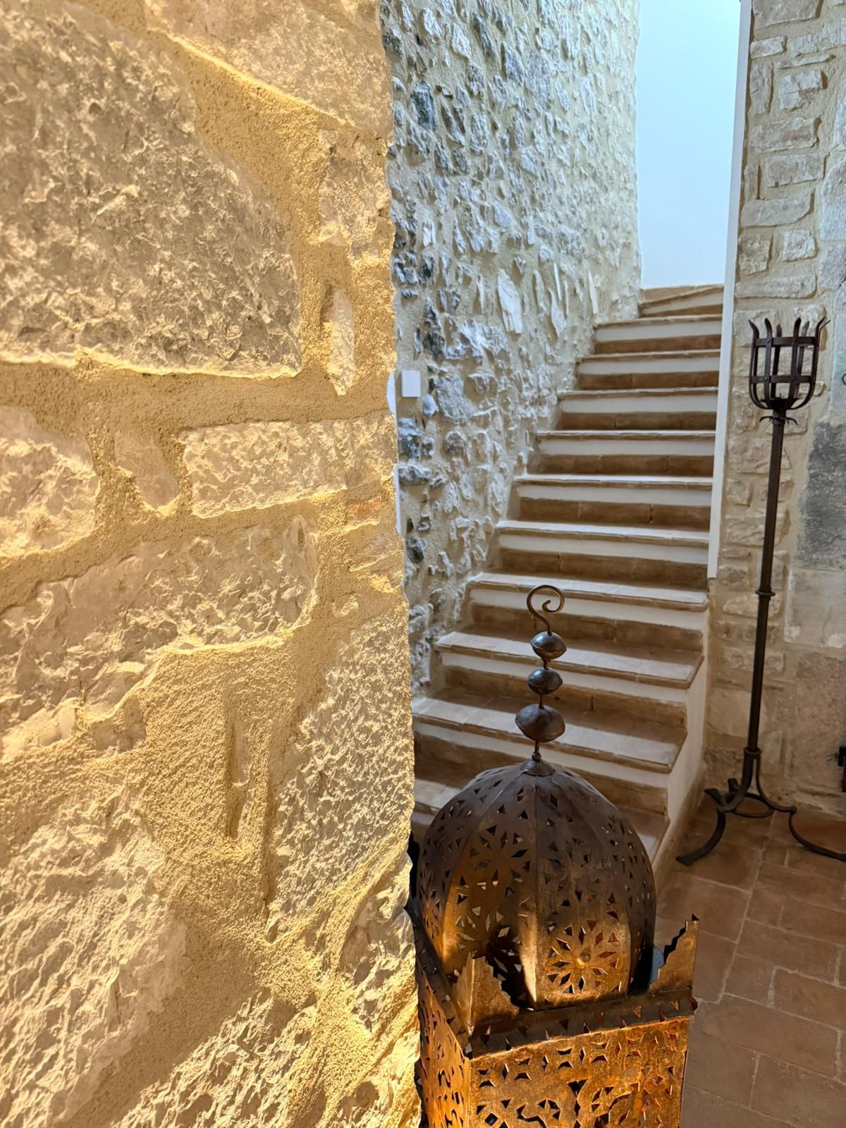 Una escalera con paredes de piedra y un farol metálico.