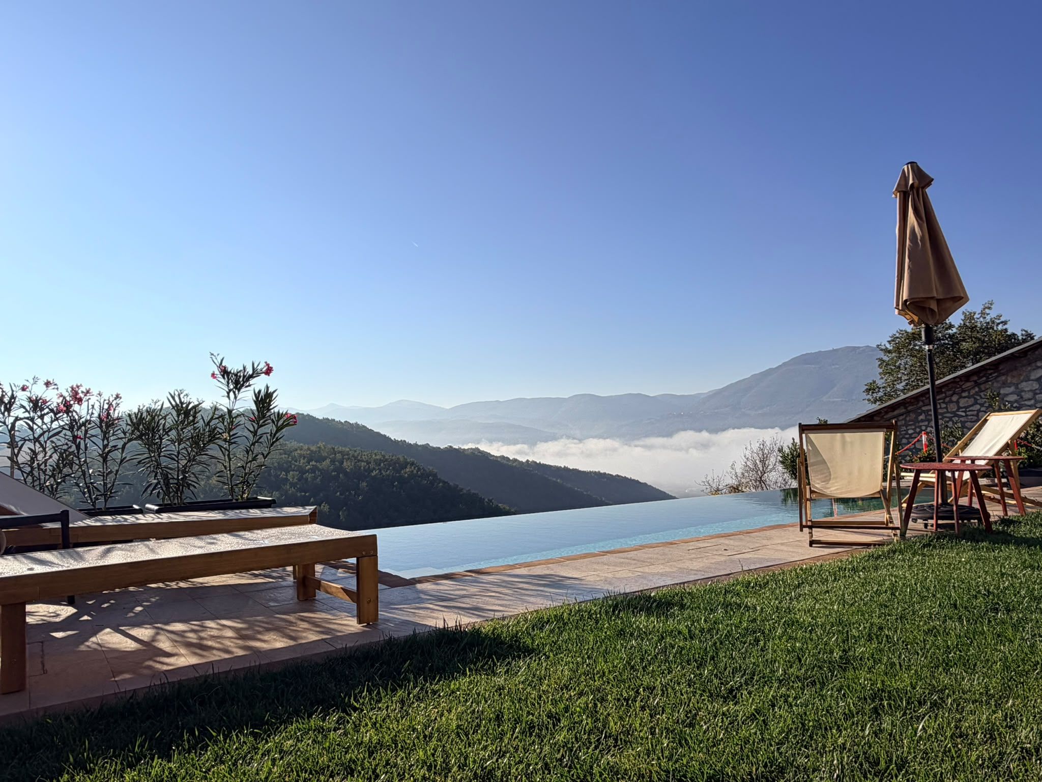 A poolside area with a view of a lake and mountains, wooden benches, and a covered seating area.
