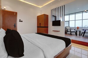 A modern hotel room with a large bed, a wardrobe, a desk with a chair, and a large window offering a city view.
