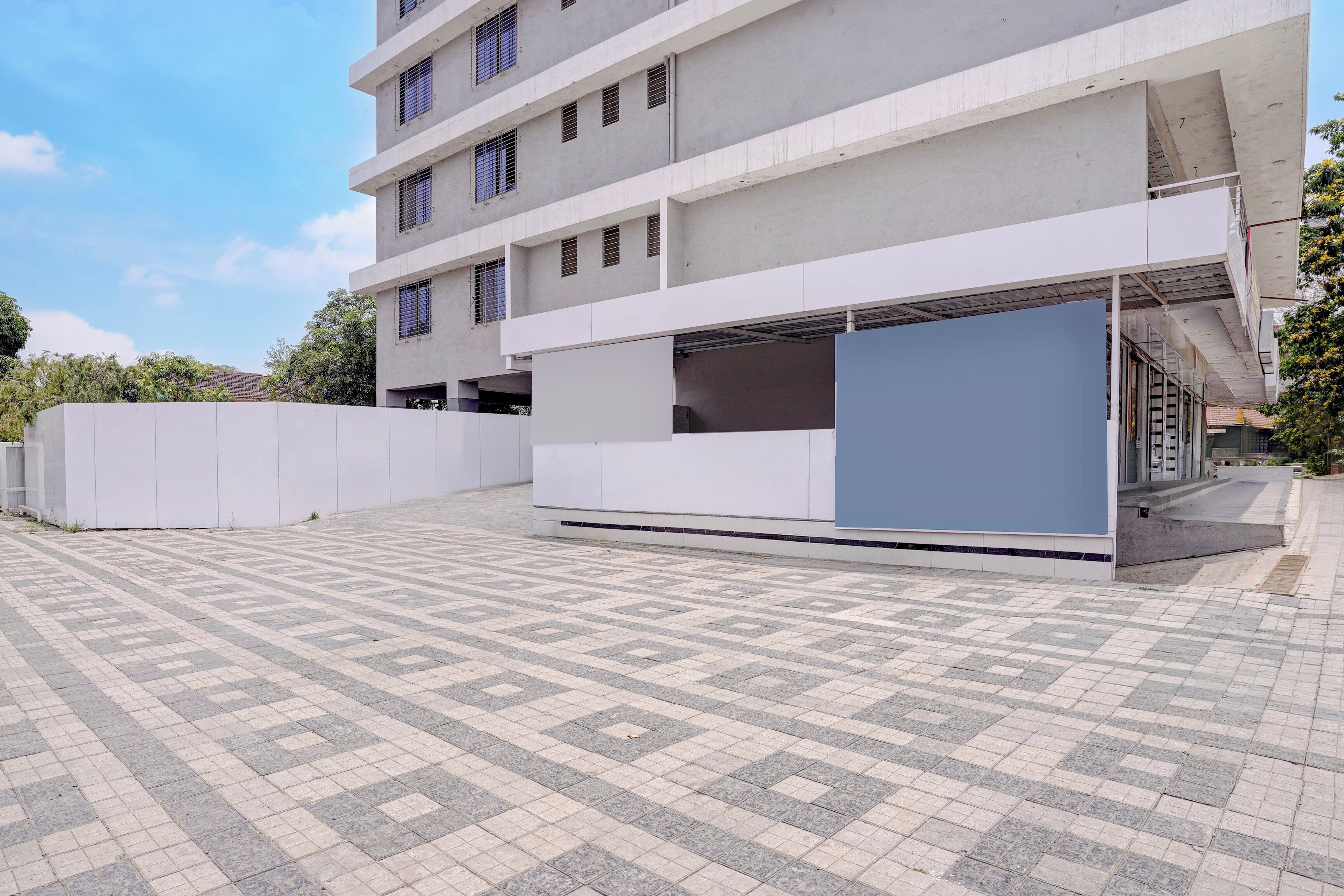 Un edificio moderno con fachada plana, varios ventanales y un área exterior cubierta con suelo estampado.