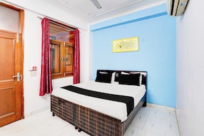Une chambre à coucher avec un lit, une porte en bois, une fenêtre avec des rideaux rouges et un mur bleu orné d’un panneau décoratif.