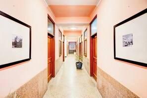 A hotel corridor with framed pictures on the walls, wooden doors, and a potted plant in the center. - Hotel O The Swarnim (Noida)
