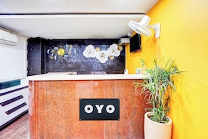 Un comptoir d’accueil avec une enseigne « OYO », une horloge murale et une plante en pot.