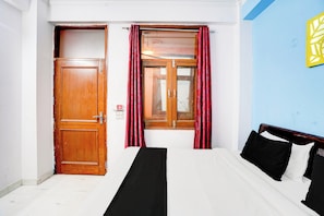 Une chambre à coucher avec un lit, une porte en bois, une fenêtre avec des rideaux et un mur orné d’un motif jaune.