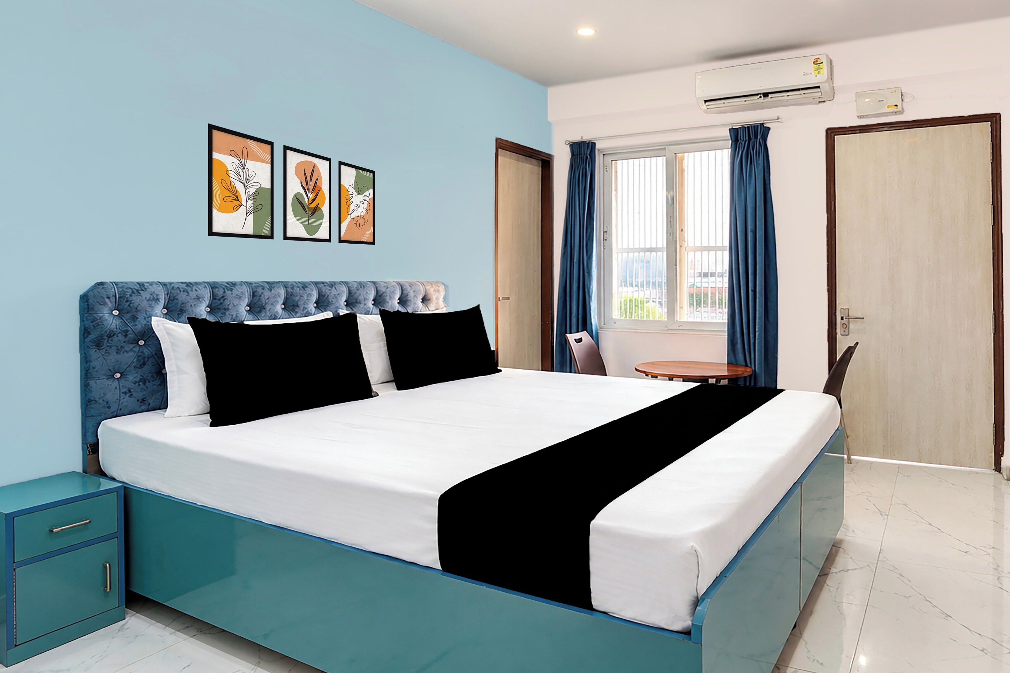 A modern bedroom with a large bed, a bedside table, a small round table, and a window with curtains.