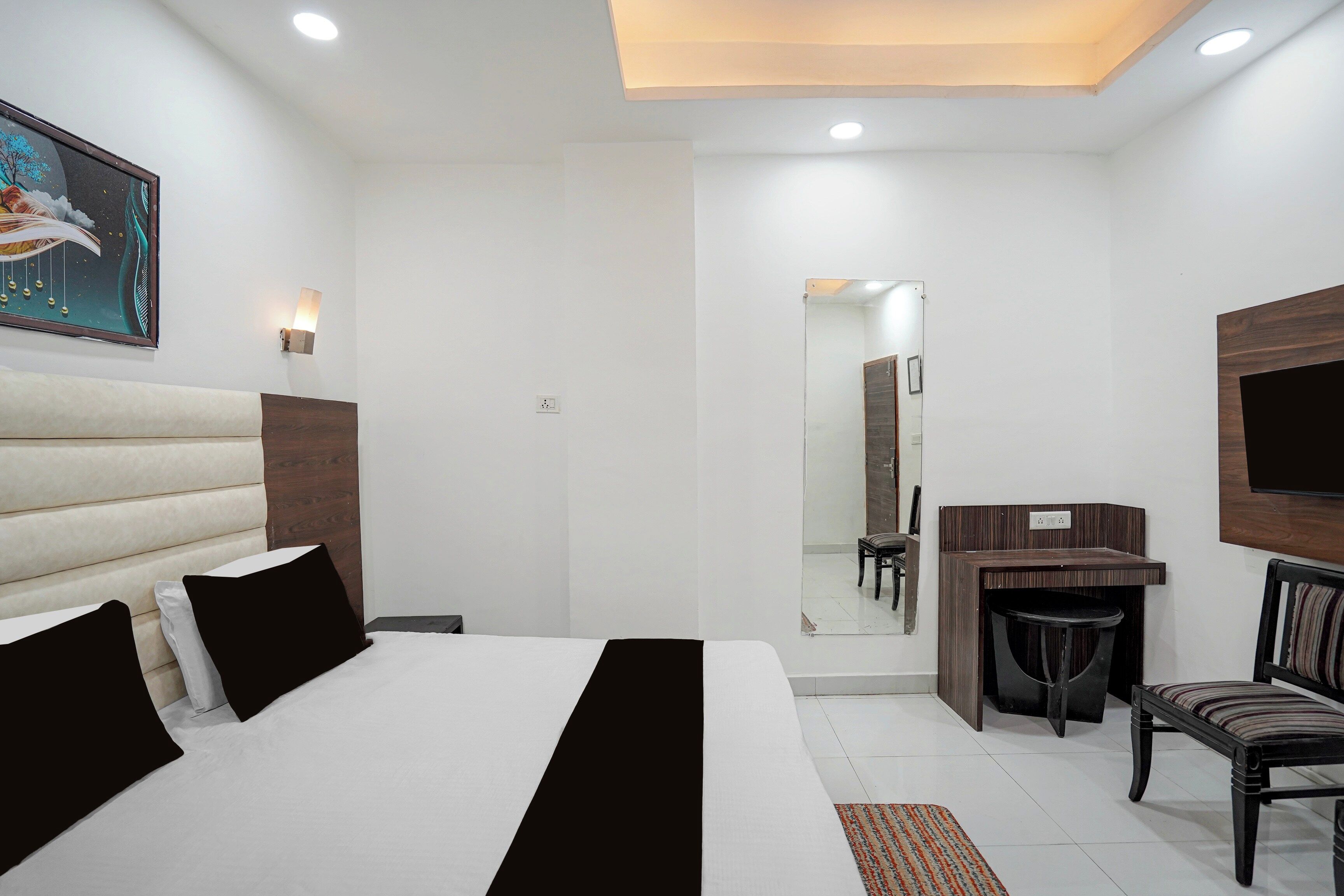 Quarto de hotel com cama, escrivaninha, cadeira, espelho e televisão.