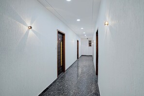 A corridor with white walls, wooden doors, and a speckled floor. - Hotel O Opal Greater Noida (Greater Noida)