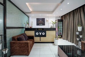 A hotel reception area with a reception desk labeled 'OYO,' a brown sofa, a coffee machine, and a wall-mounted fan. - Hotel O Opal Greater Noida (Greater Noida)