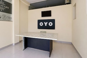 A room with a table, a wall-mounted sign with 'OYO' text, and a wall with a logo and icons. - Hotel O Prime Stay (Noida)