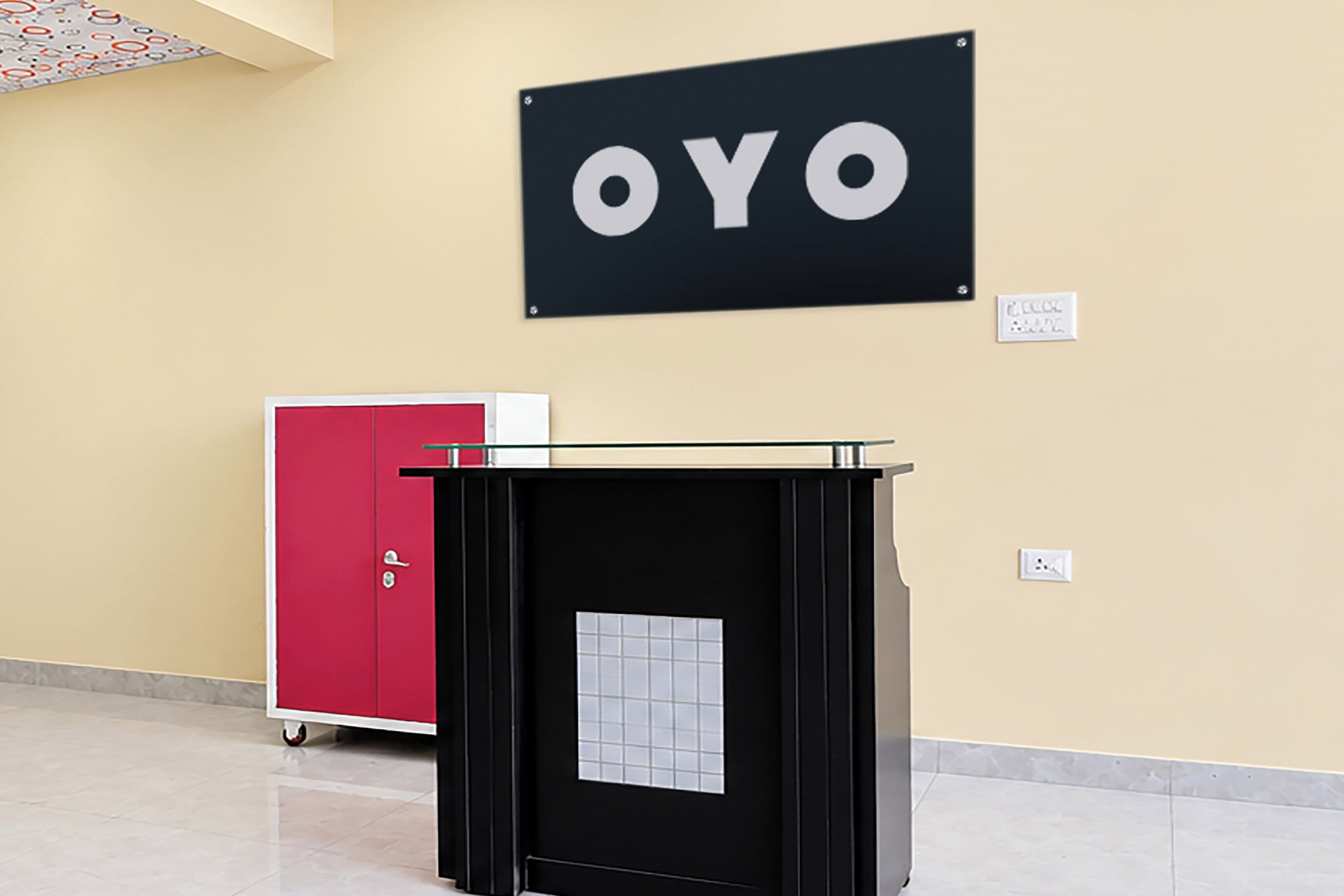 Un área de recepción con un mostrador negro, un armario rojo y un letrero en la pared con las letras 'OYO'.