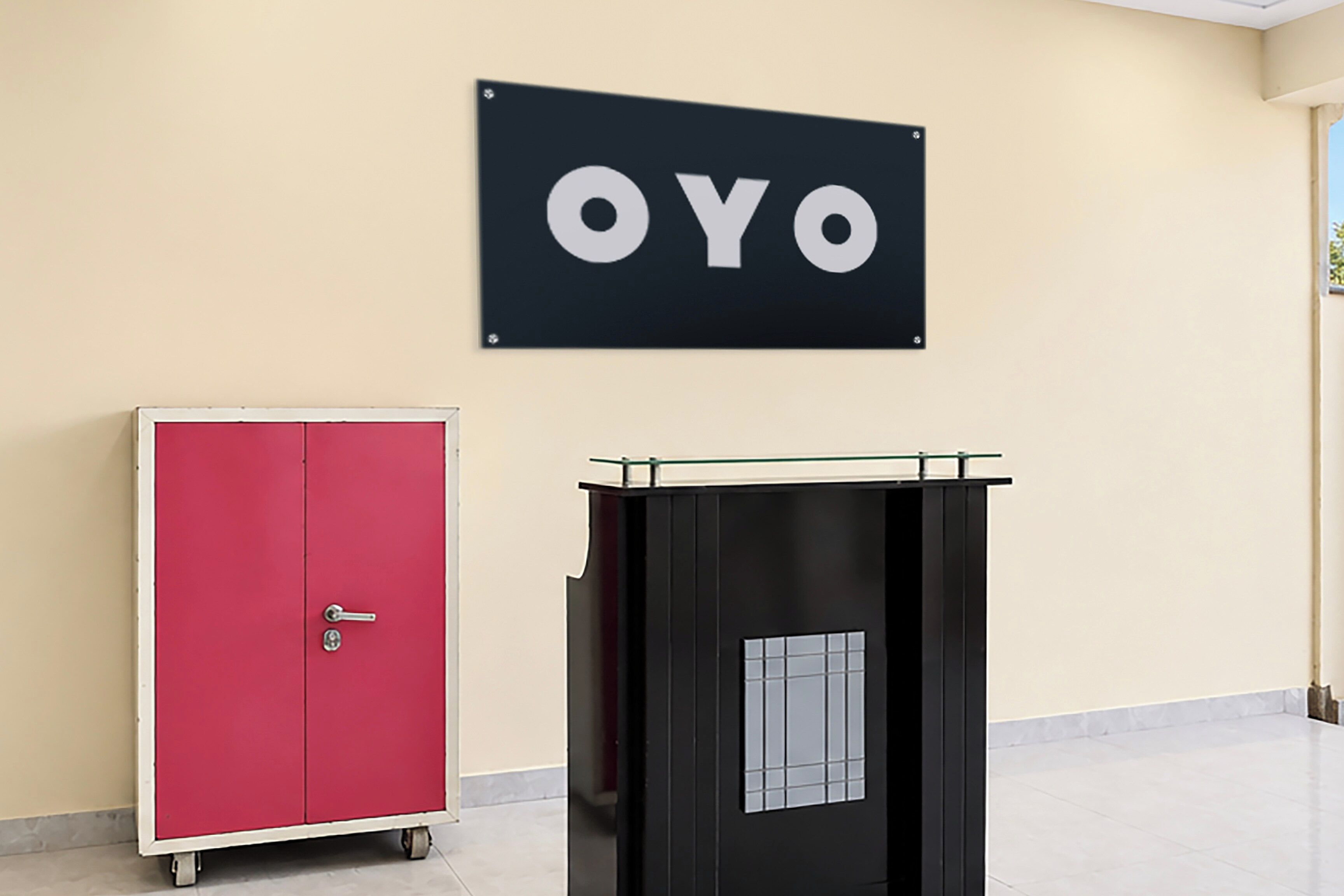 Un armario rojo y un carrito utilitario negro en una habitación con pared color beige y un letrero que dice 'OYO'.