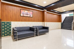 Un área de recepción con pared de madera, un cuadro enmarcado de caballos, un sofá de cuero negro y una escalera.