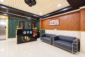 Un área de recepción con mostrador negro que muestra la marca 'OYO', una pared de madera con un cuadro enmarcado y un sofá gris.