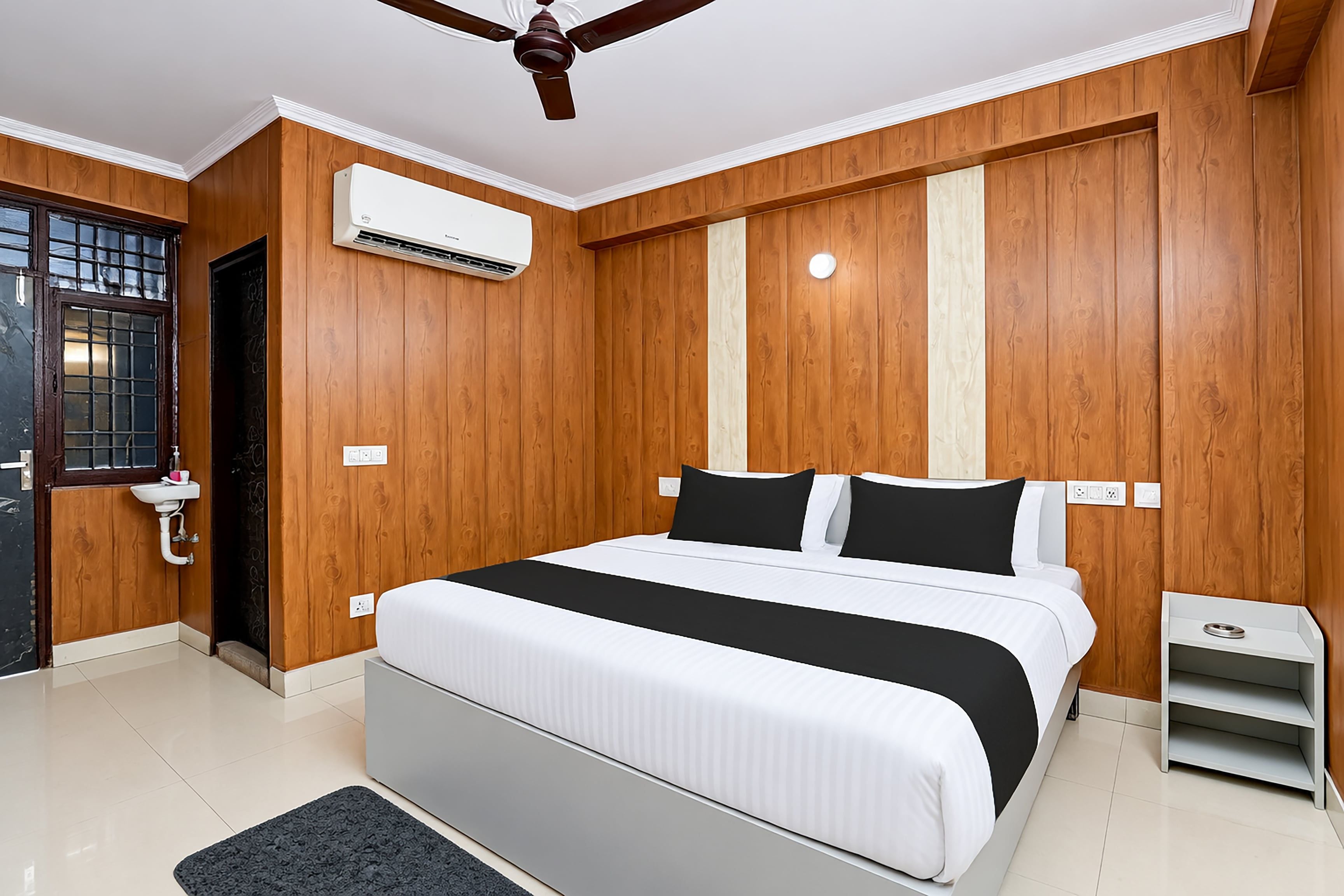 Un dormitorio con cama, mesita de noche, una pequeña mesa, ventilador de techo y aire acondicionado.