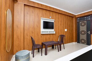 Una habitación con paredes de madera, un televisor de pantalla plana montado en la pared, una pequeña mesa con dos sillas y un otoman redondo.