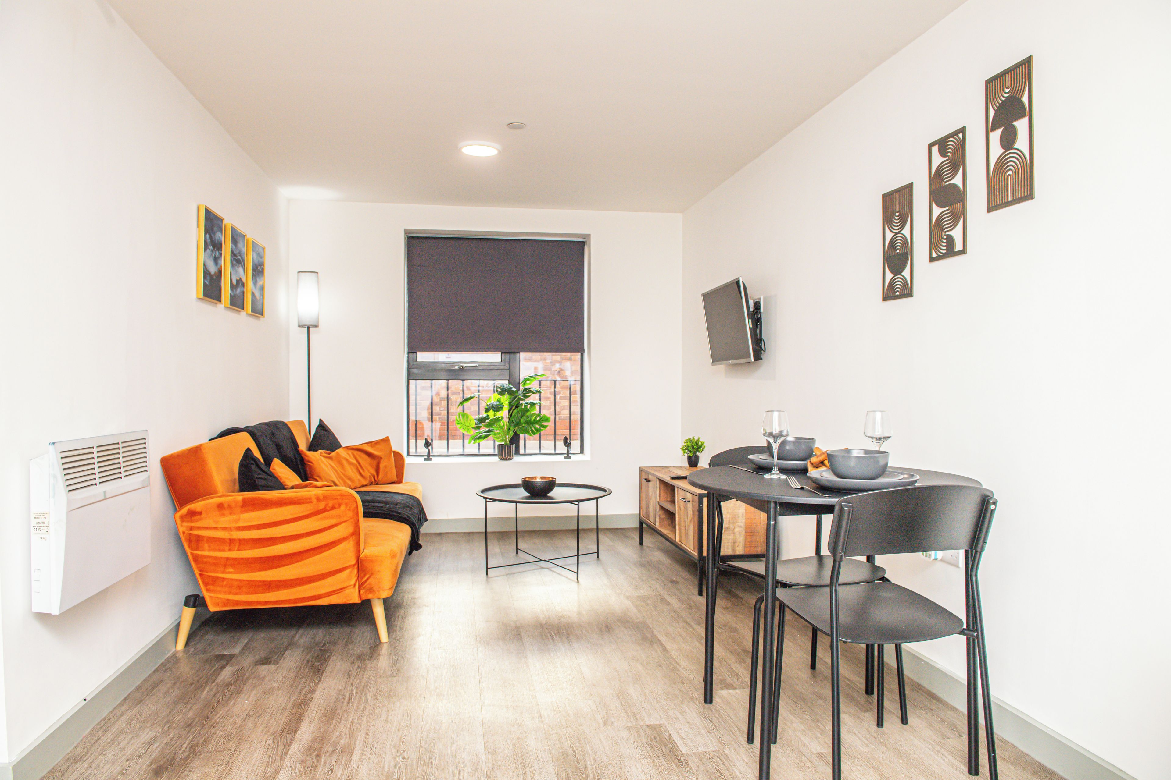Ein modernes Wohnzimmer mit einer Couch, einem Esstisch mit Stühlen, einem kleinen Beistelltisch und einer Zimmerpflanze.