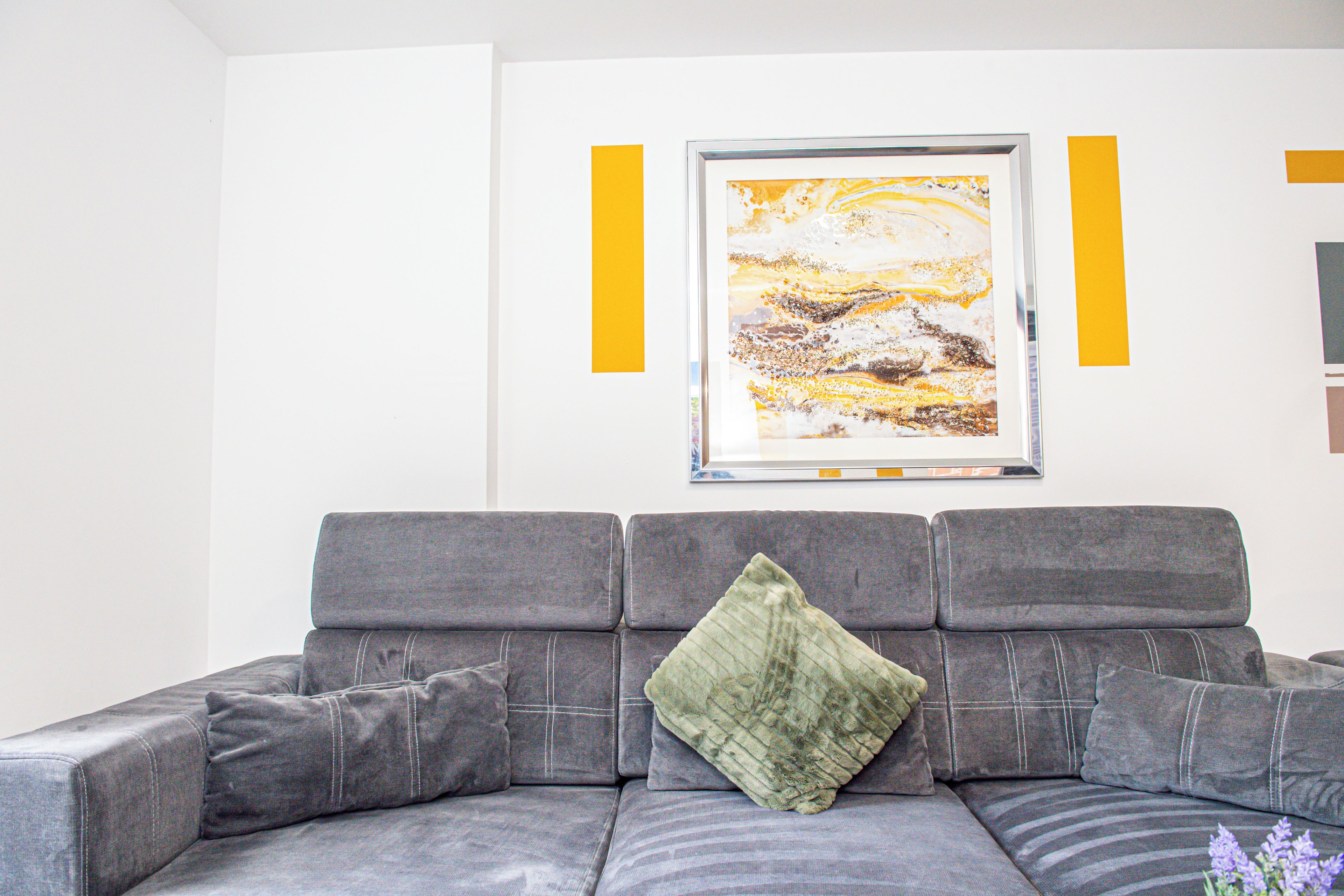 Ein graues Sofa mit einem grünen Kissen und einem gerahmten abstrakten Gemälde an der Wand.