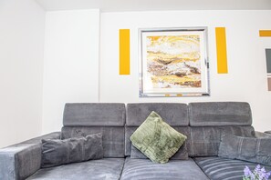 Un sofà gris amb un coixí verd i un quadre abstracte amb marc a la paret.