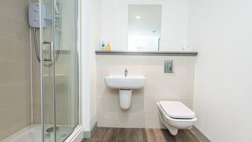 Un baño moderno con cabina de ducha de vidrio, un lavamanos blanco y un inodoro.