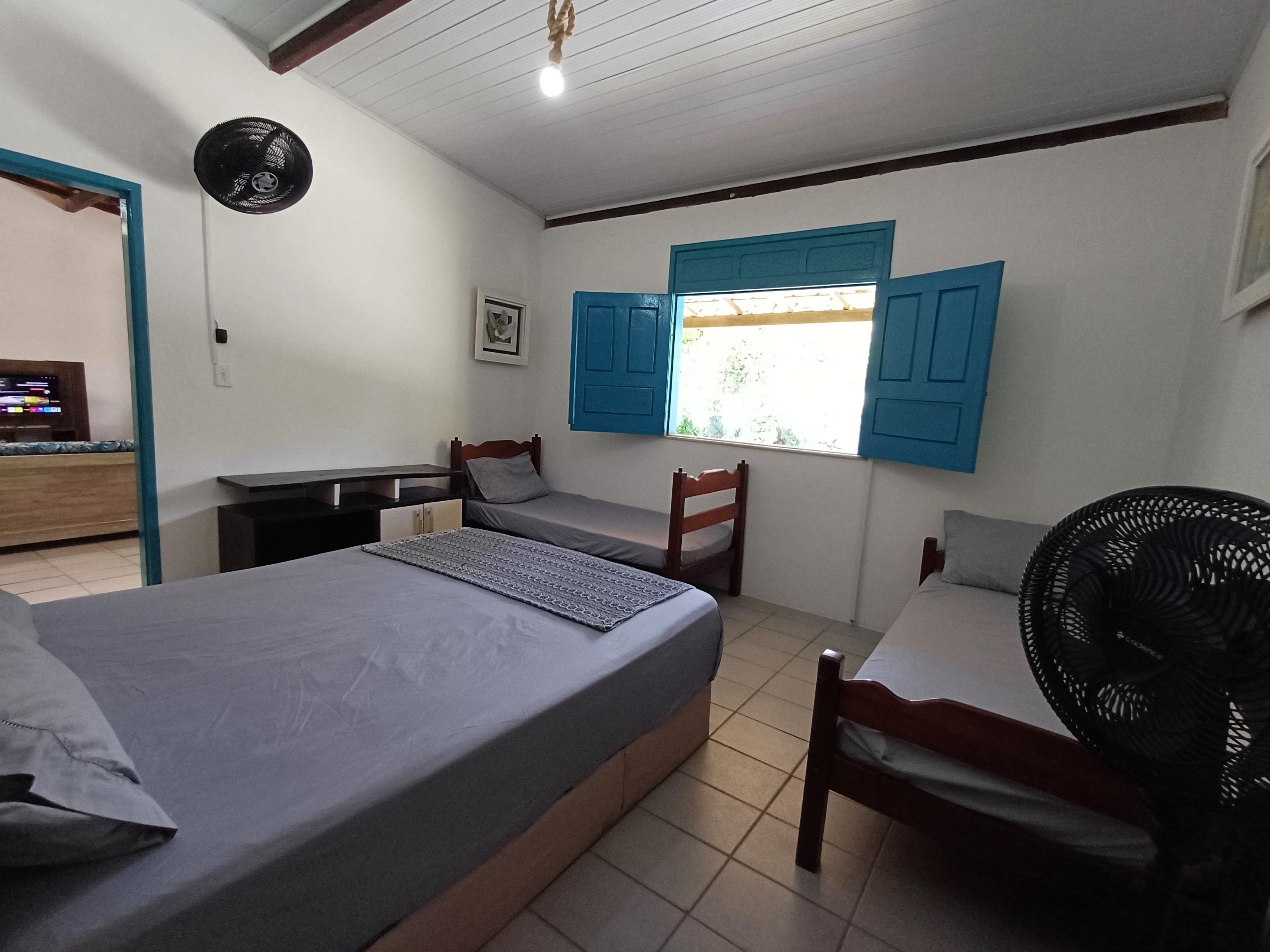 Una habitación con cama, escritorio, silla, ventana con persianas azules y un ventilador.