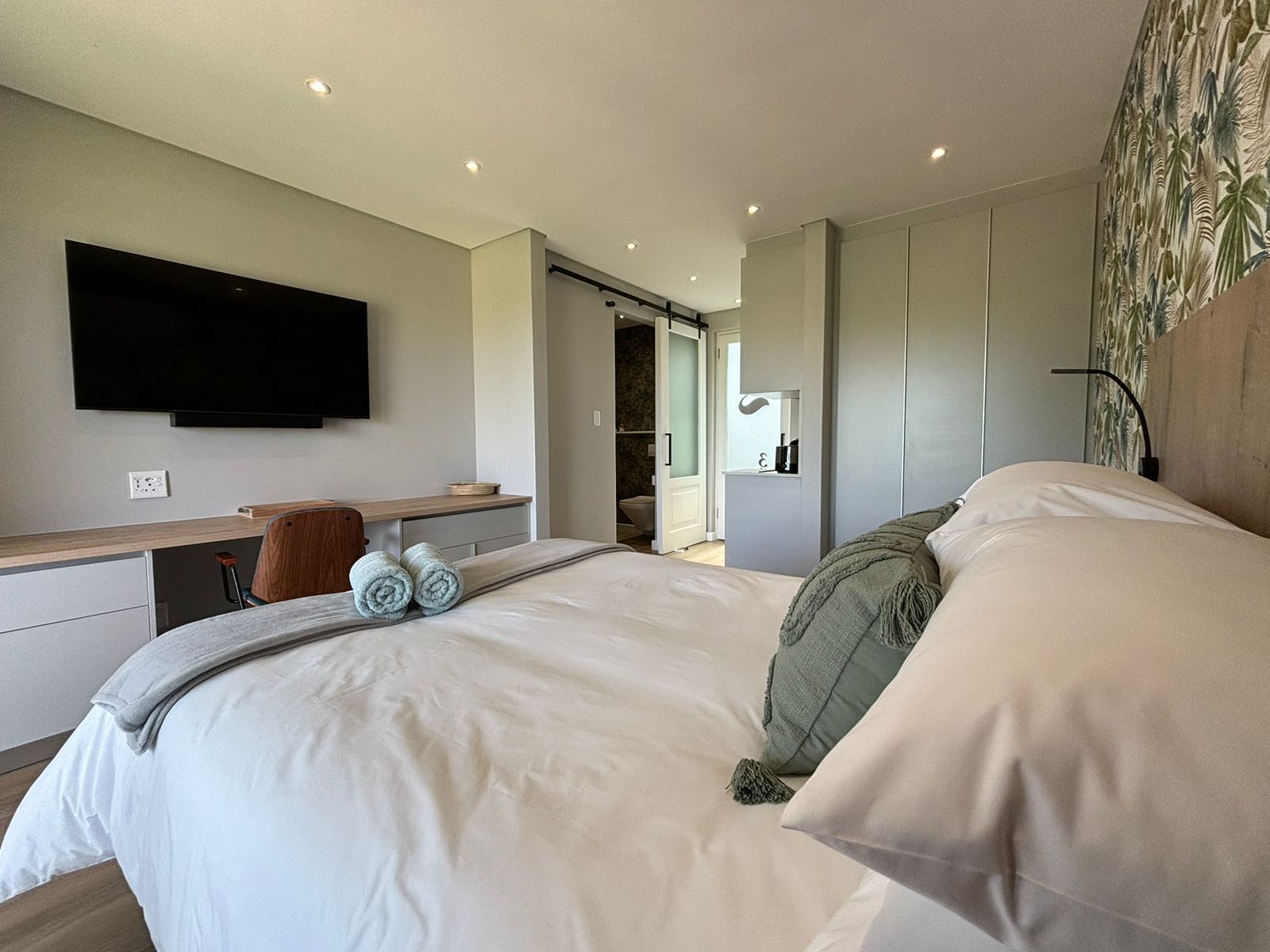 Una habitación de hotel moderna con una cama grande, un televisor de pantalla plana en la pared, un escritorio con una silla y un vestidor.
