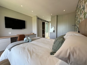 A modern hotel room with a large bed, a flat-screen TV mounted on the wall, a desk with a chair, and a walk-in closet. - Swanemeer Apartments (Cape Town)
