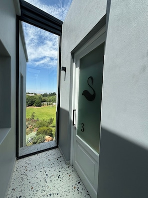 A narrow hallway with a door marked with the number 3, leading to a balcony with a view of a green landscape. - Swanemeer Apartments (Cape Town)