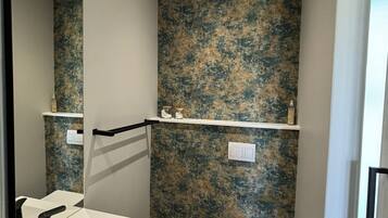 A bathroom with a white sink, a toilet, and a mirror. There are shelves above the toilet and a light switch on the wall.