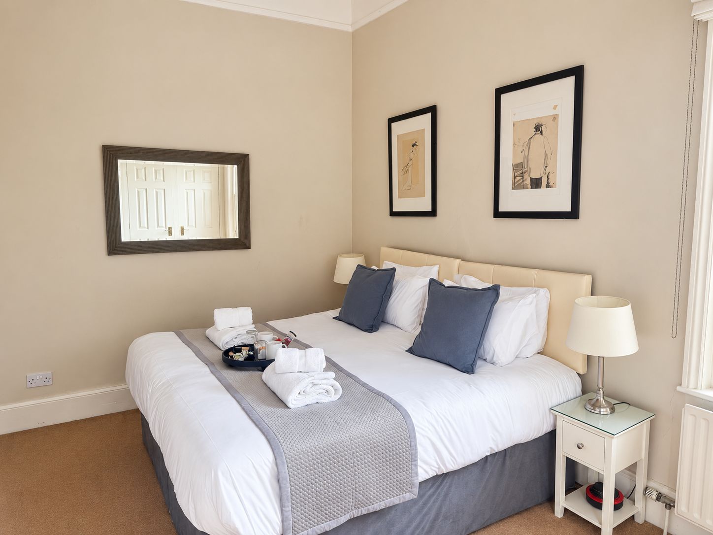 Une chambre d’hôtel avec un lit, une table de chevet avec une lampe et deux tableaux encadrés au mur.