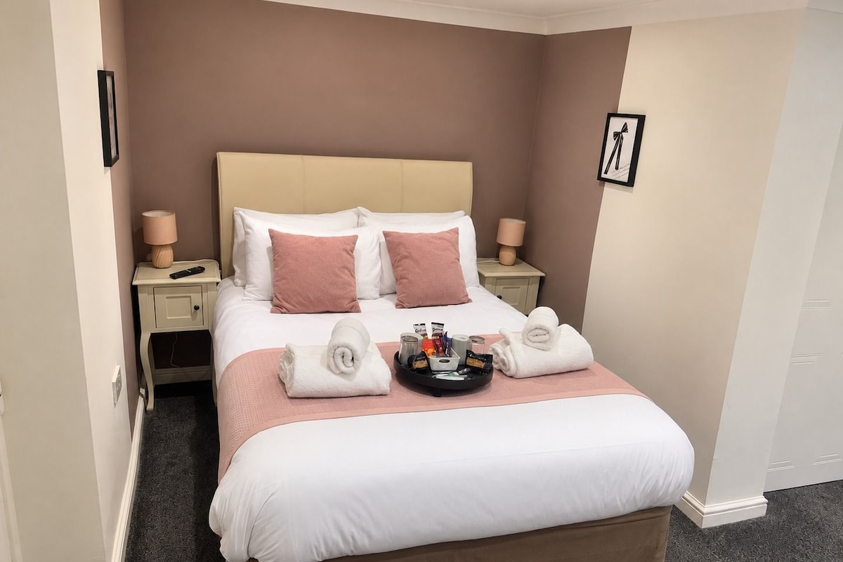 Habitación de hotel con una cama, mesitas de noche, un atril con artículos de aseo y un cuadro en la pared.