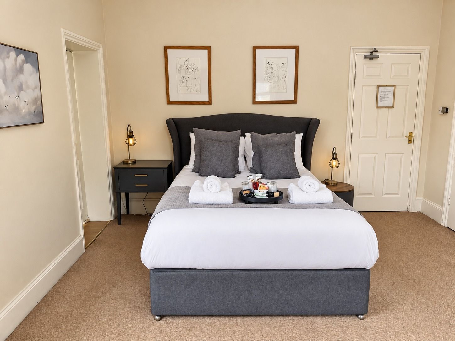 A neatly made bed with a dark headboard, two bedside tables with lamps, and a door with a sign.