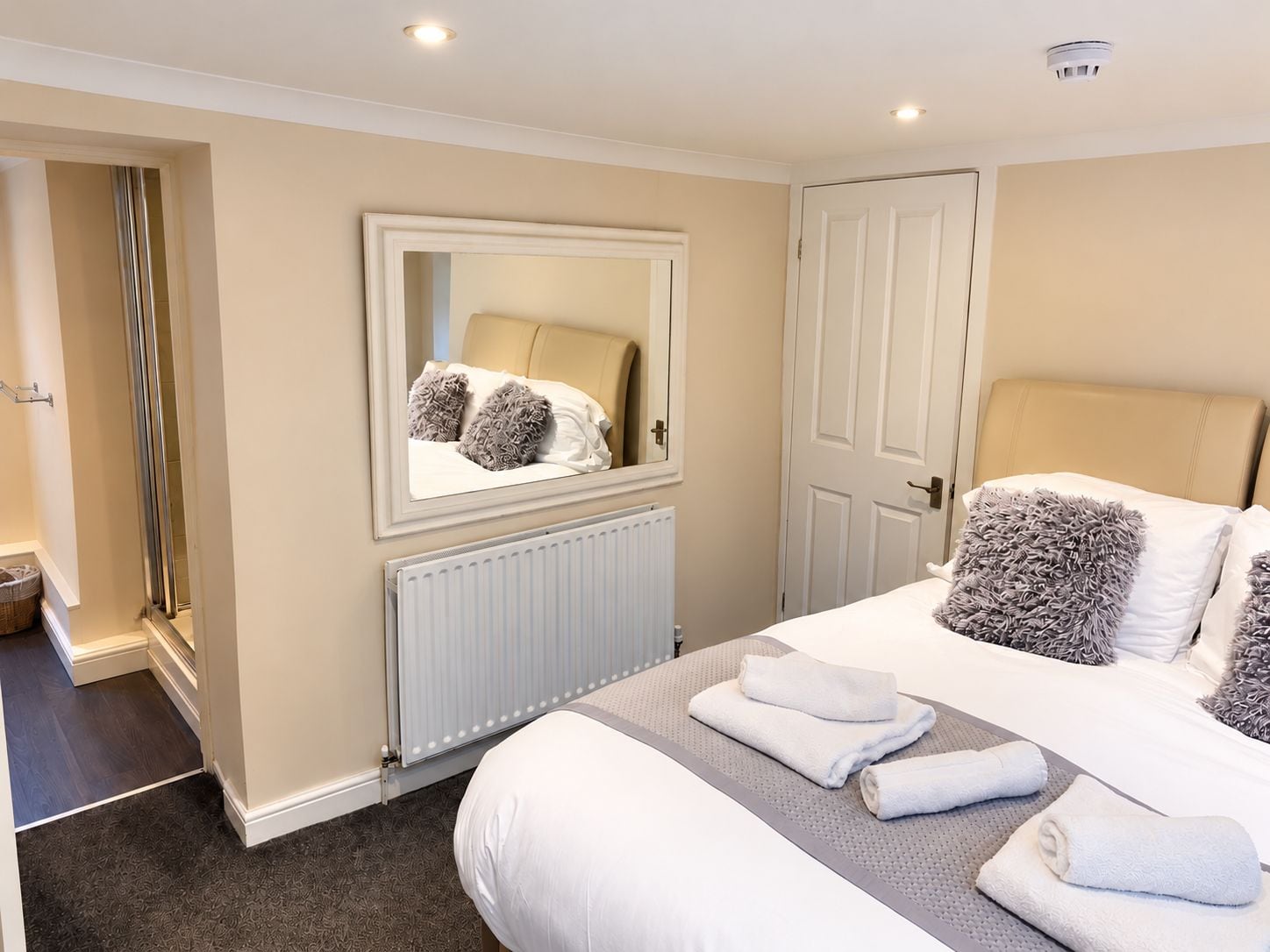 A hotel room with a bed, a mirror, a door, and a radiator.