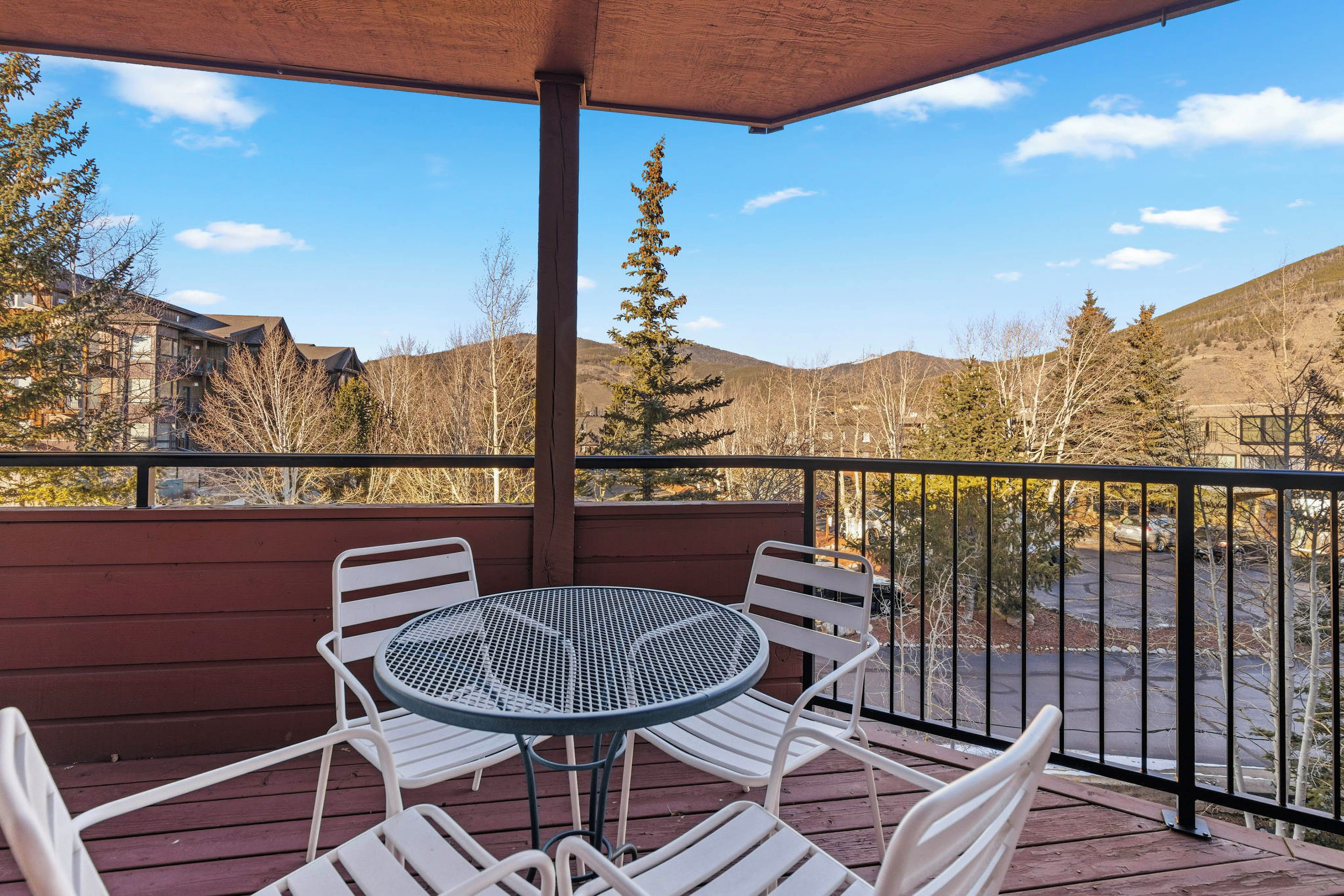 A balcony with a round table and four chairs, overlooking a parking area and a mountainous landscape.