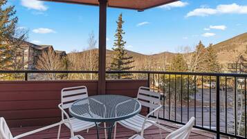 A balcony with a round table and four chairs, overlooking a parking area and a mountainous landscape.