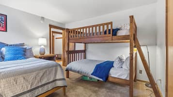 A bunk bed room with a wooden ladder, a bedside table with a lamp, and a framed picture on the wall.