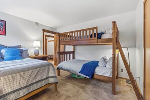 Quarto com beliche, uma escada de madeira, mesa de cabeceira com abajur e quadro na parede.