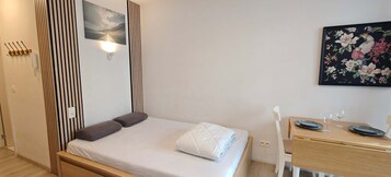 Un dormitorio con cama, mesita de noche con lámpara, un cuadro y teléfono.