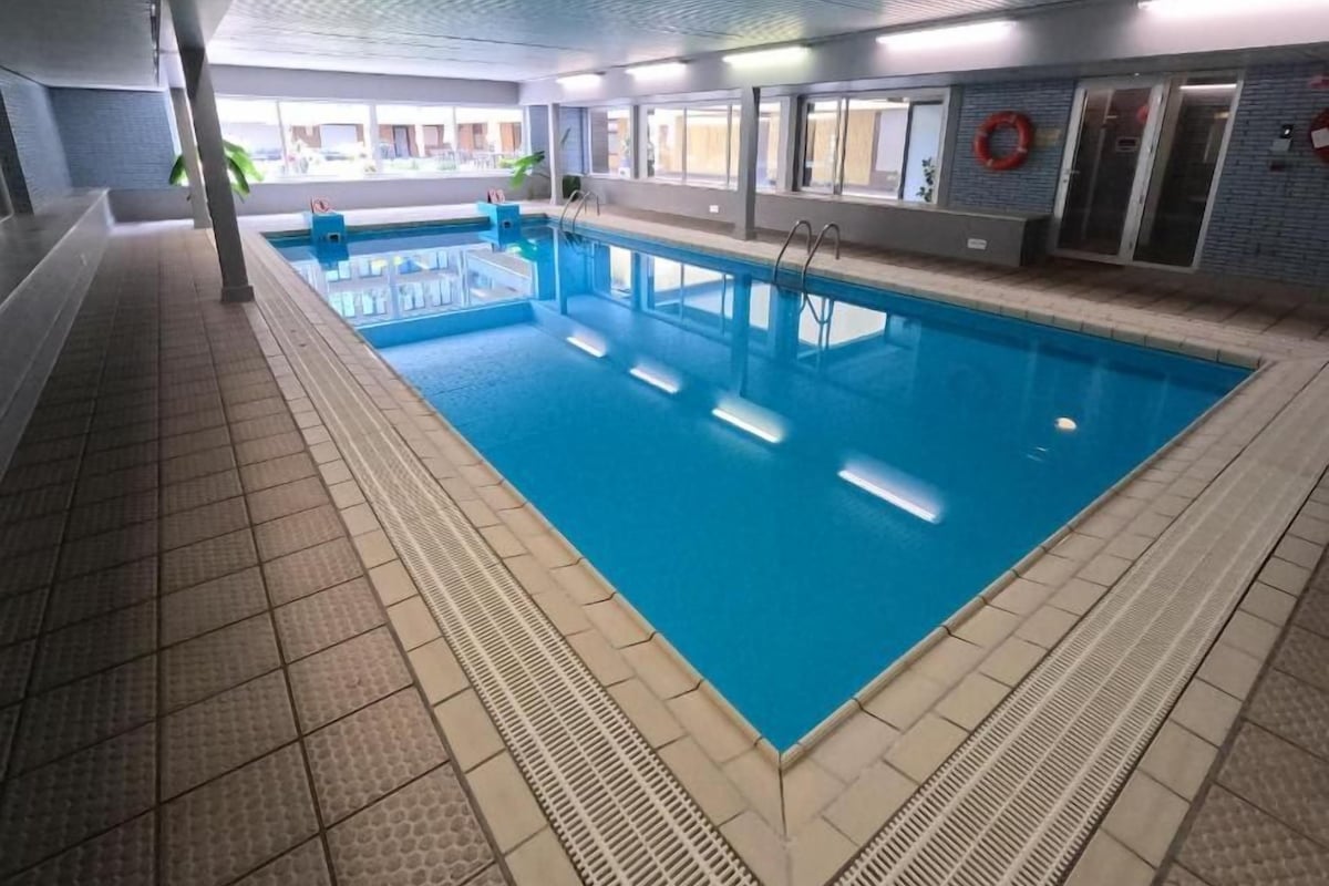 Piscina interna com água cristalina, piso ladrilhado e equipamentos de segurança.
