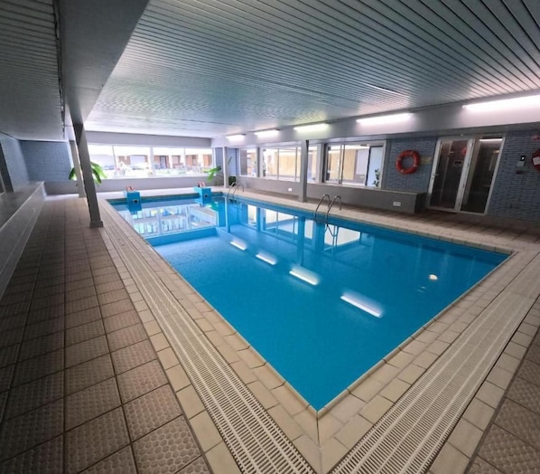 Piscina interna com água cristalina, piso ladrilhado e equipamentos de segurança.