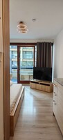 Quarto com uma cama, uma TV sobre um suporte de madeira, uma porta de vidro deslizante para uma varanda e uma luminária de teto.