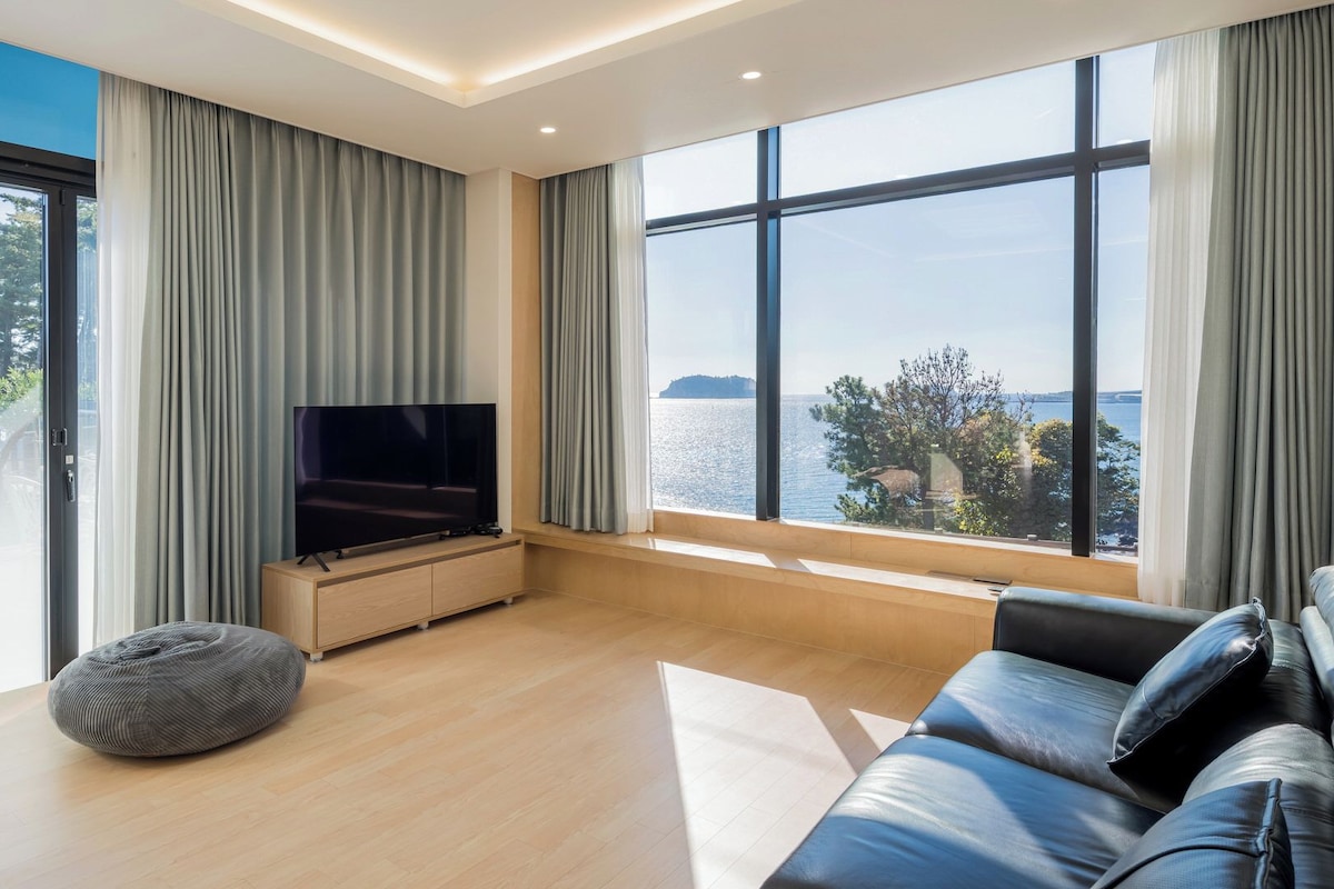 Ein modernes Wohnzimmer mit großem Fernseher, bequemen Sitzmöglichkeiten und Meerblick.