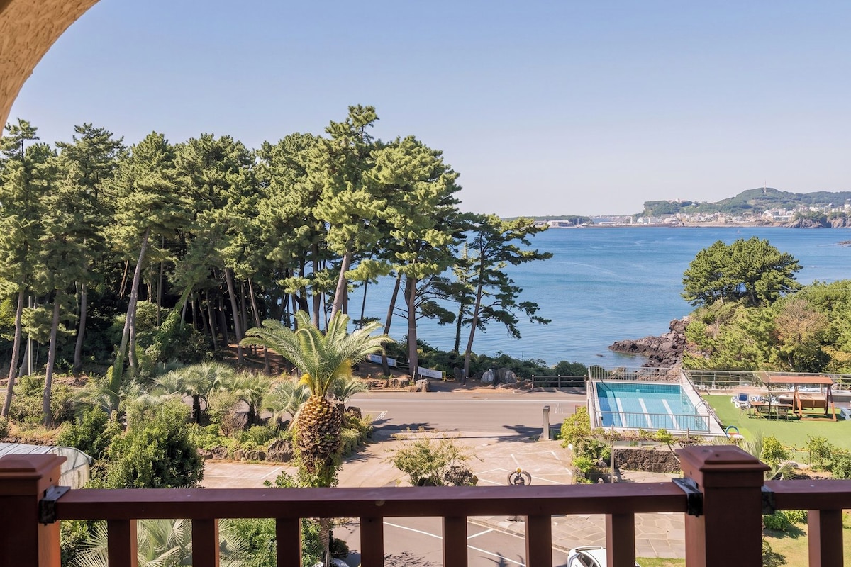 Ein Balkon mit Blick auf eine Küstenlandschaft, einen Parkplatz und ein Schwimmbad.