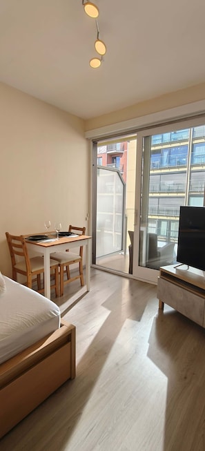 Quarto de hotel com cama, escrivaninha, cadeira, televisão e porta de vidro corrediça que dá para uma varanda externa.