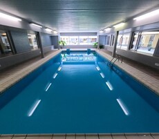 Piscina interna com pistas demarcadas, cercada por paredes com janelas e chão revestido com azulejos.