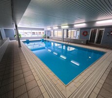 Piscina interna com água cristalina, piso ladrilhado e equipamentos de segurança.