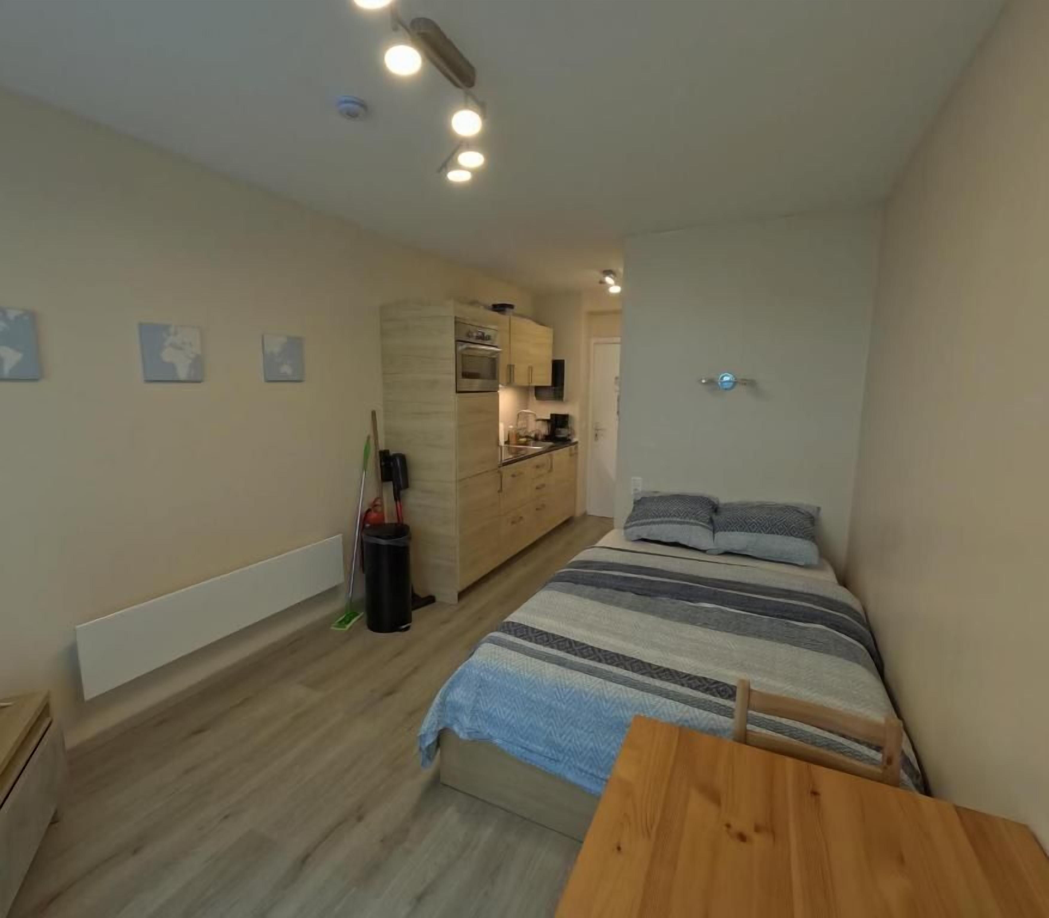 Une chambre avec un lit, une table en bois et, au fond, un coin cuisine.
