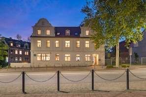Een historisch gebouw met veel ramen, een centrale ingang en een hek met kettingen ervoor.