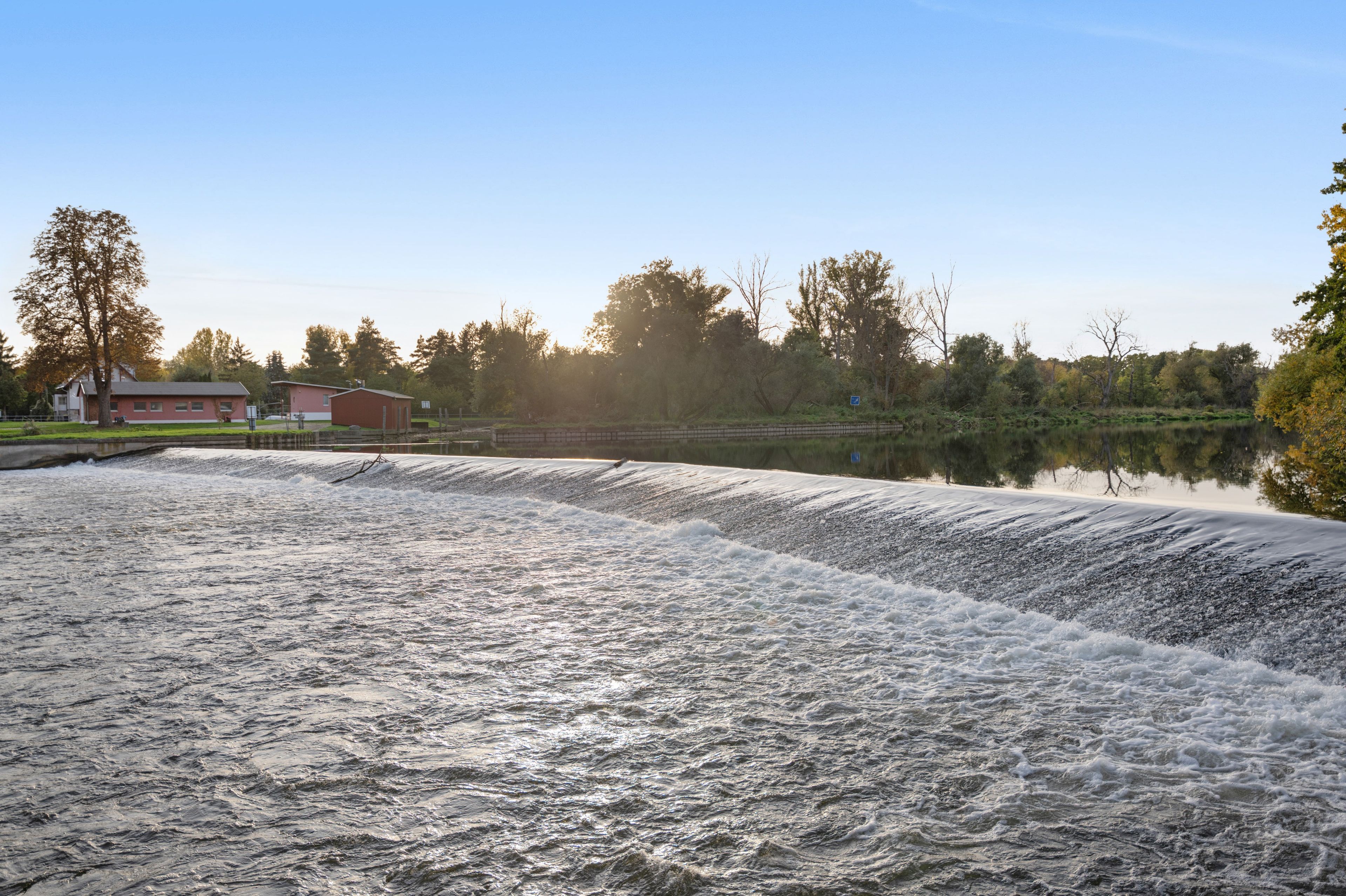Ein Stausee mit fließendem Wasser, eine Brücke und Gebäude im Hintergrund.