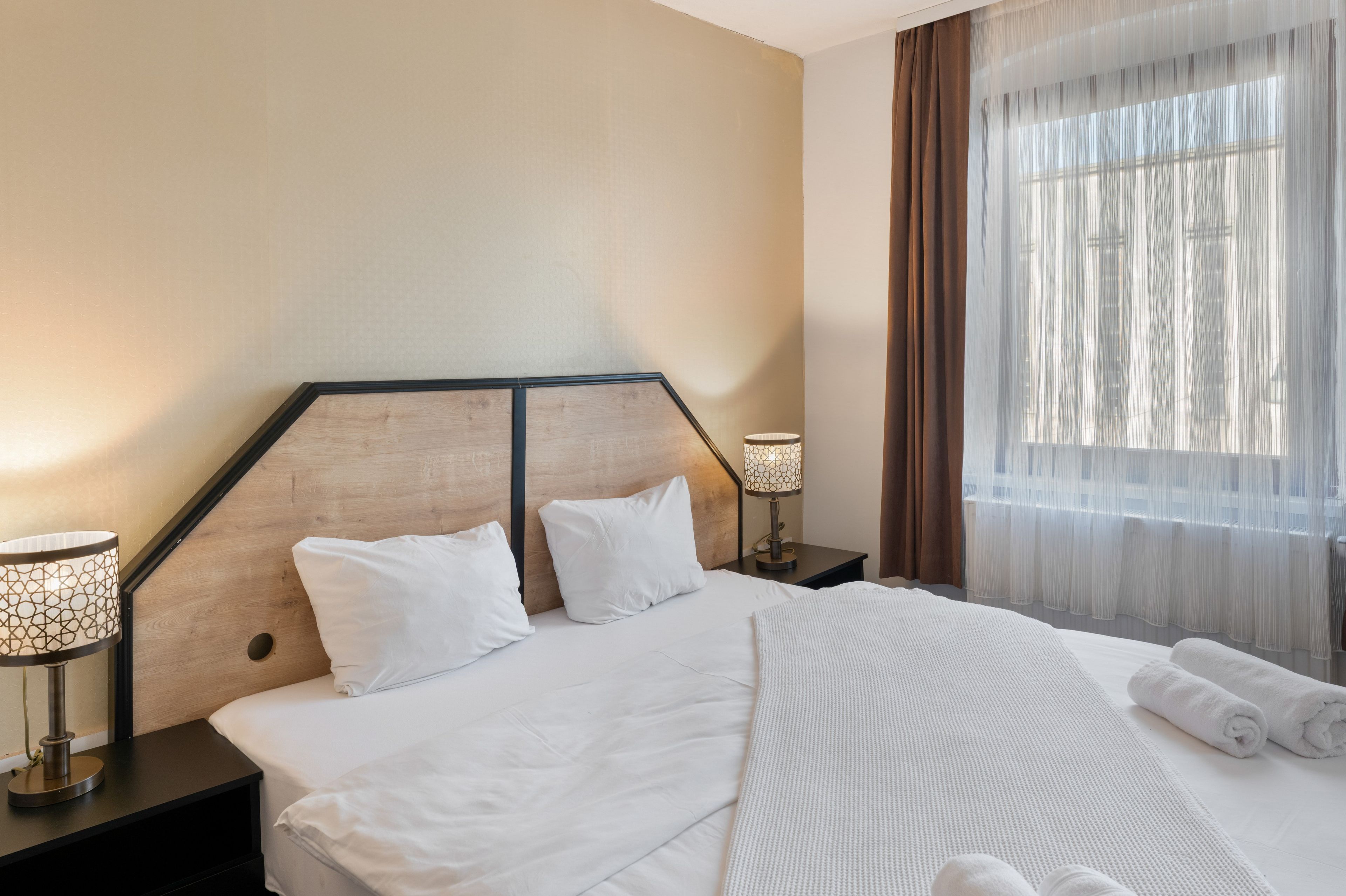 A hotel room with a large bed, two bedside tables, a lamp, and a window with curtains.
